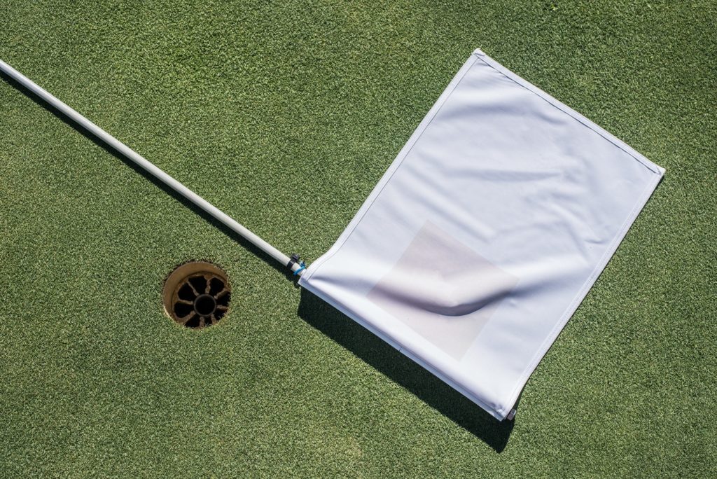 Golf field with empty hole and white flag